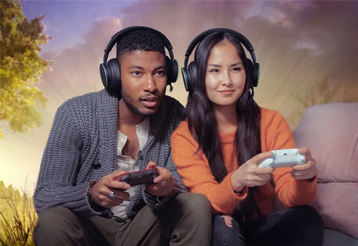 Два человека в наушниках сидят на диване и играют в Xbox вместе